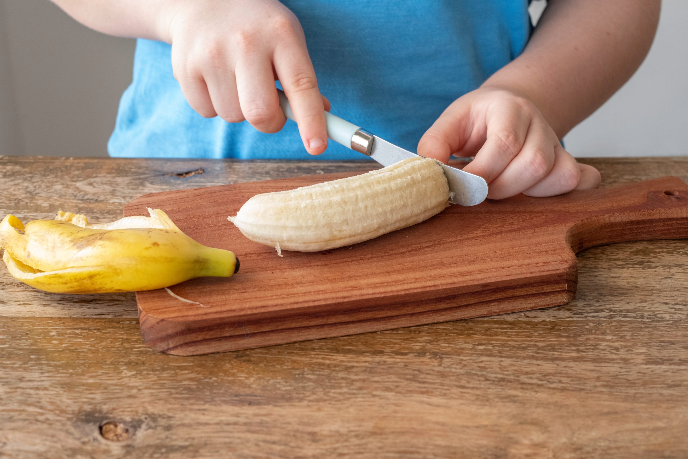 Child slicing a banana on a wooden board