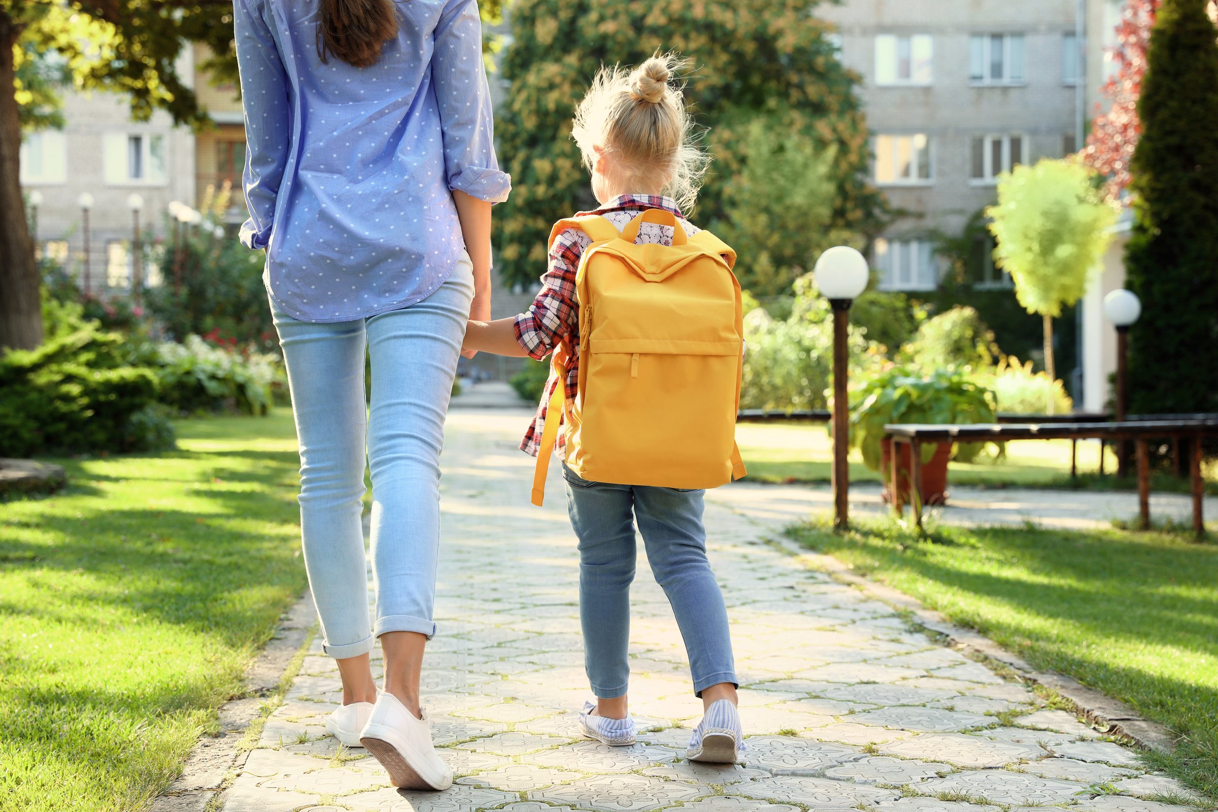Parent walking a child with a yellow backpack to school