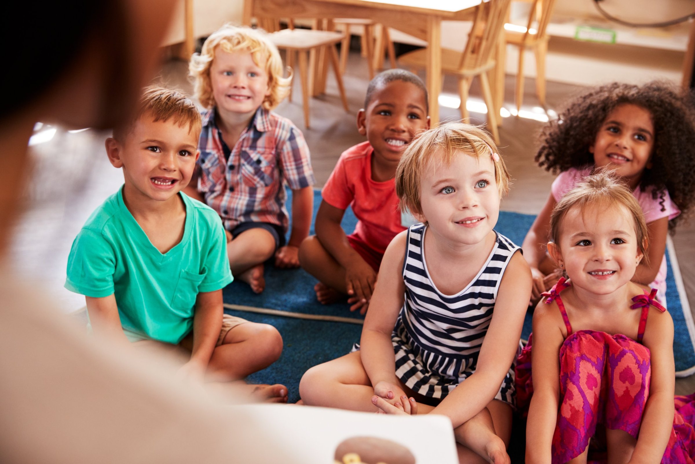 Diverse group of preschoolers listening to their educator on the classroom rug